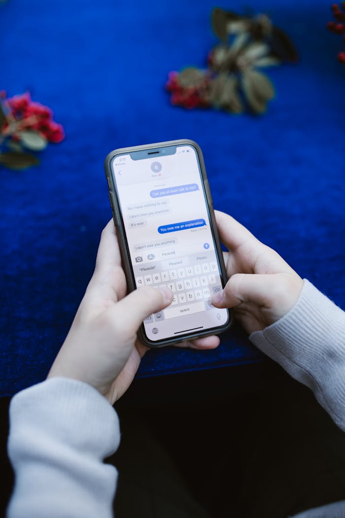 Close-up of a person sending a text message on a smartphone over a blue surface.