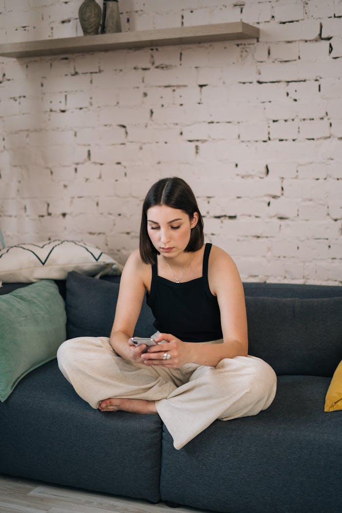 Young woman sitting comfortably on a sofa using smartphone in a chic living room setting.